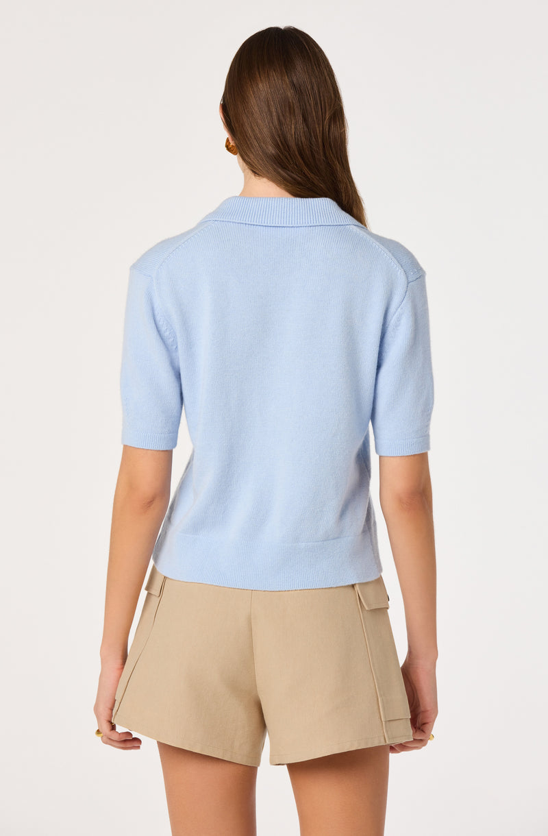 Woman in a light blue short-sleeve sweater and beige shorts, back view.