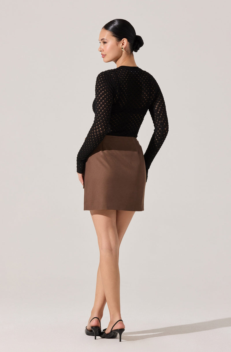 A woman is wearing a black long-sleeve knitted top with a see-through, open-weave pattern, paired with a high-waisted brown skirt that has a smooth, solid fabric. She is also wearing black high-heeled sandals.