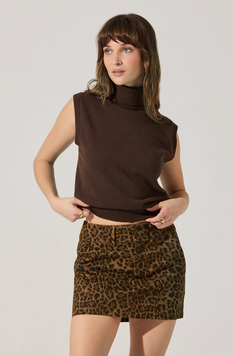 A woman is wearing a sleeveless, dark brown turtleneck top paired with a high-waisted, leopard print skirt.