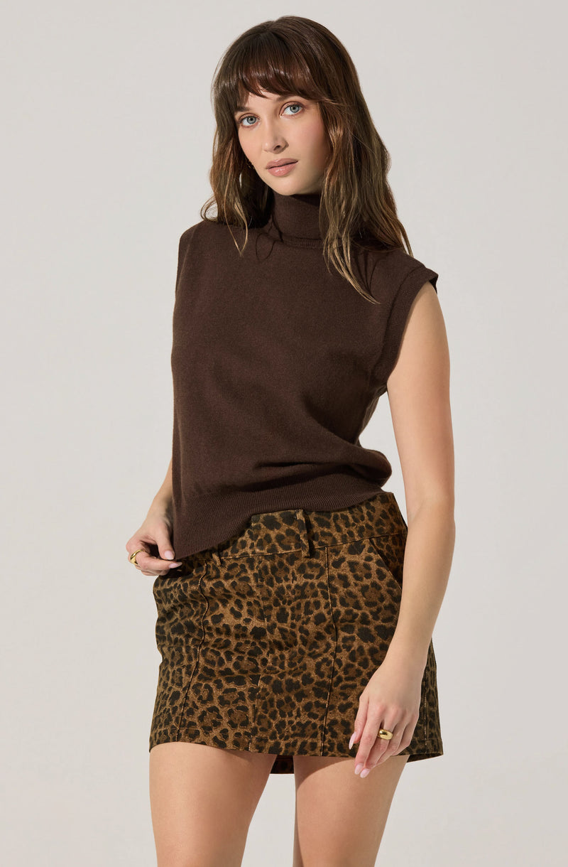 A woman is wearing a sleeveless, dark brown turtleneck top paired with a short, leopard print skirt in shades of brown and black.