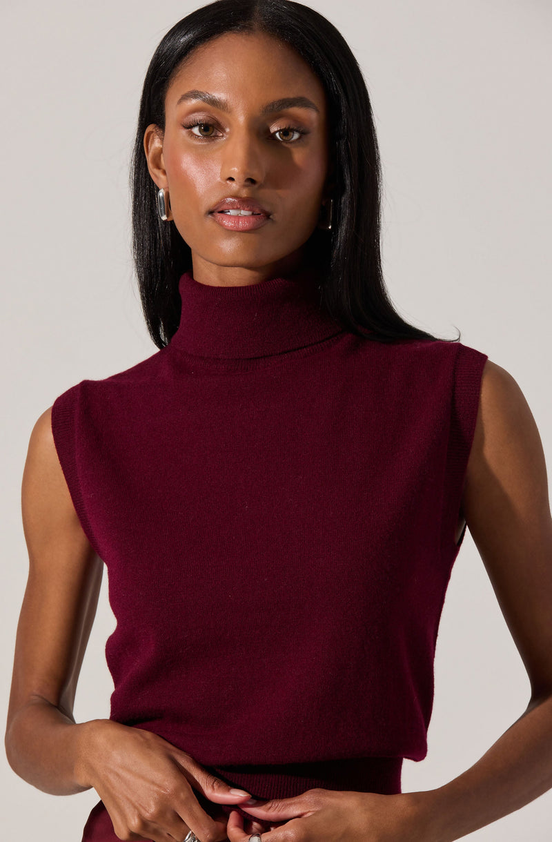 A woman wearing a sleeveless, high-neck sweater in a deep burgundy color.