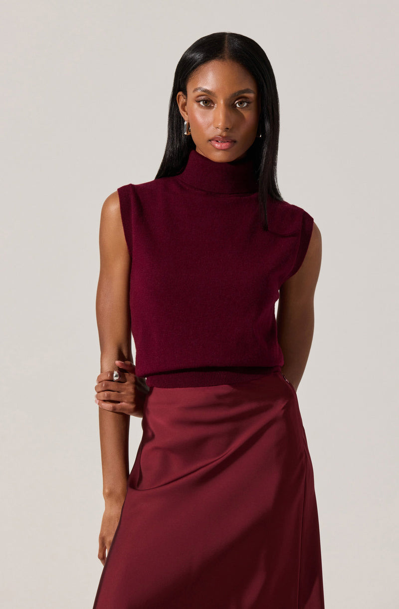 A woman is wearing a sleeveless, high-neck, burgundy knit top paired with a shiny, satin-like burgundy skirt.