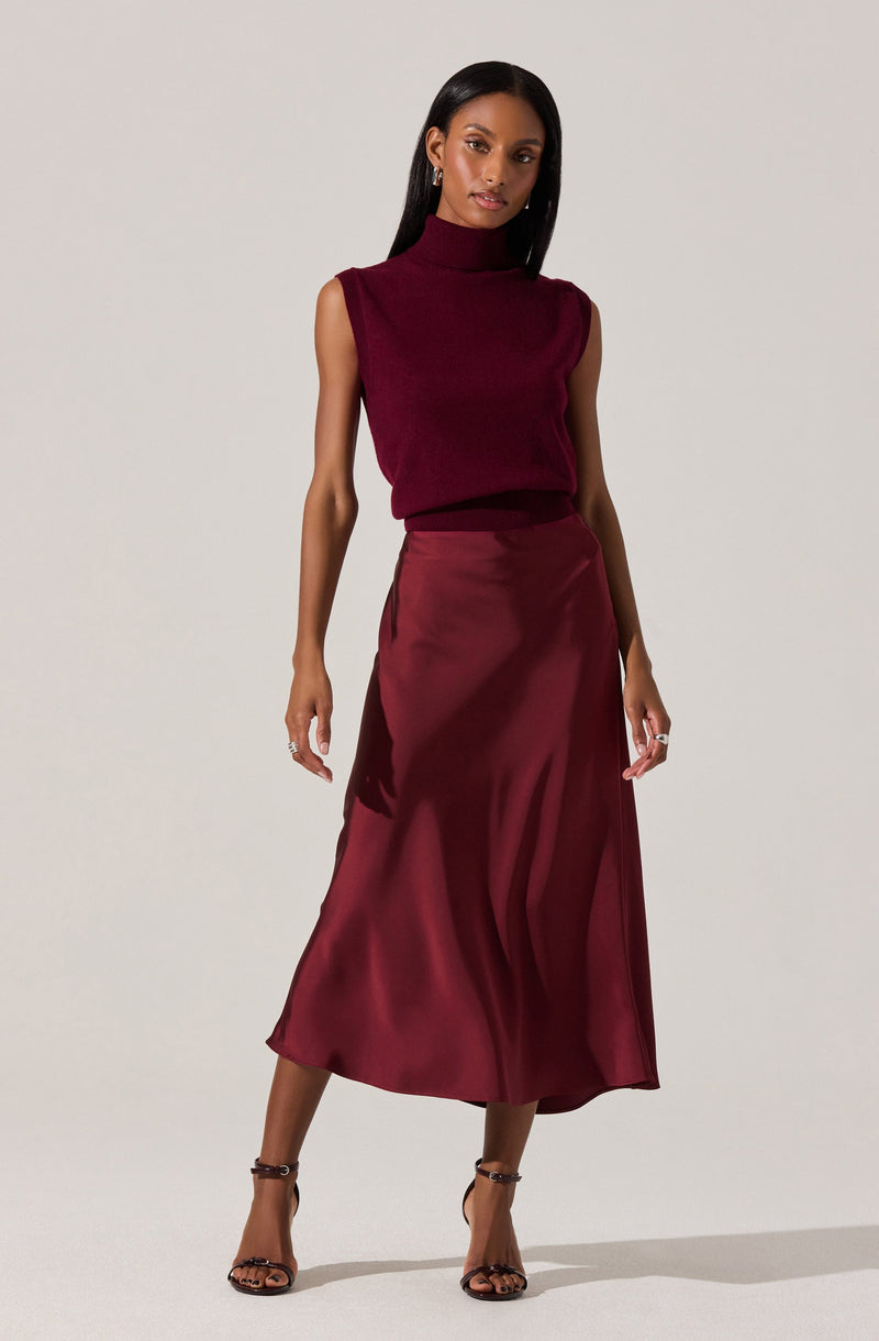 A woman is wearing a sleeveless, high-neck, burgundy knit top paired with a shiny, matching burgundy satin midi skirt.
