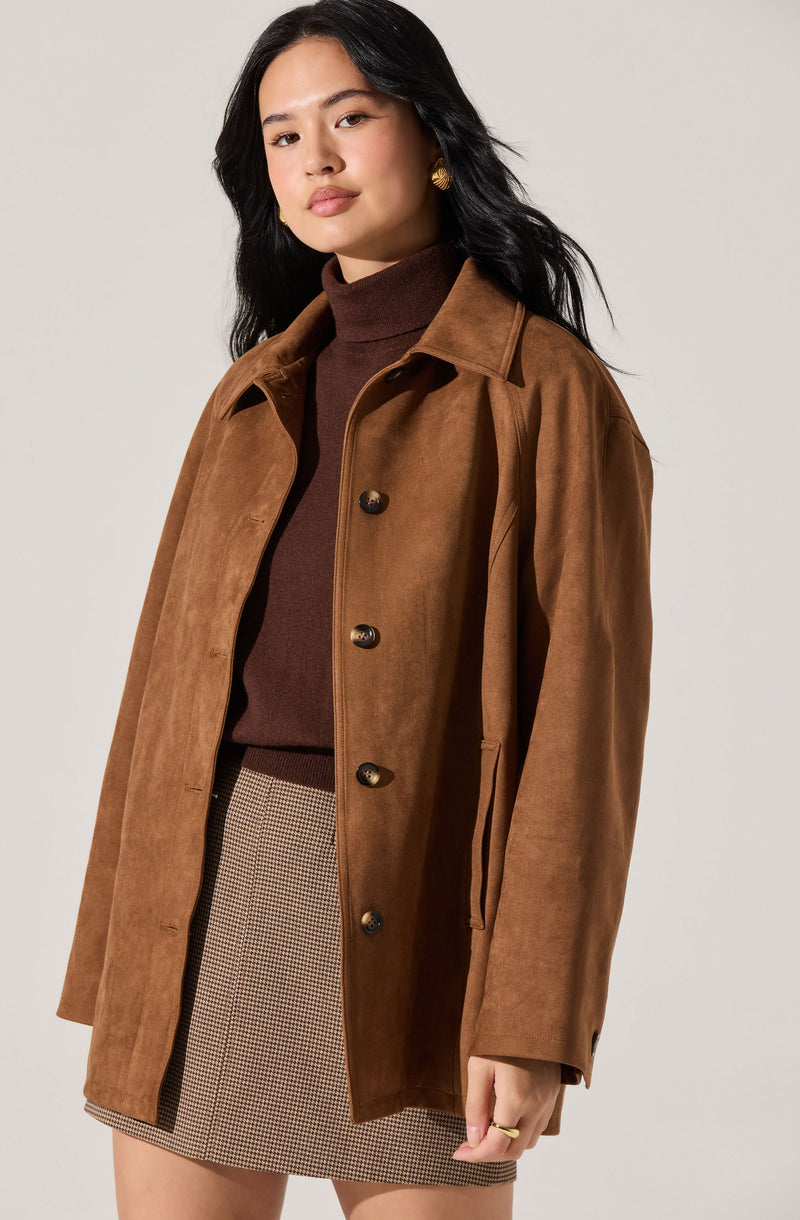 A woman is wearing a brown suede button-up coat with a classic collar, layered over a dark brown turtleneck sweater. She pairs this with a beige and brown houndstooth patterned skirt.