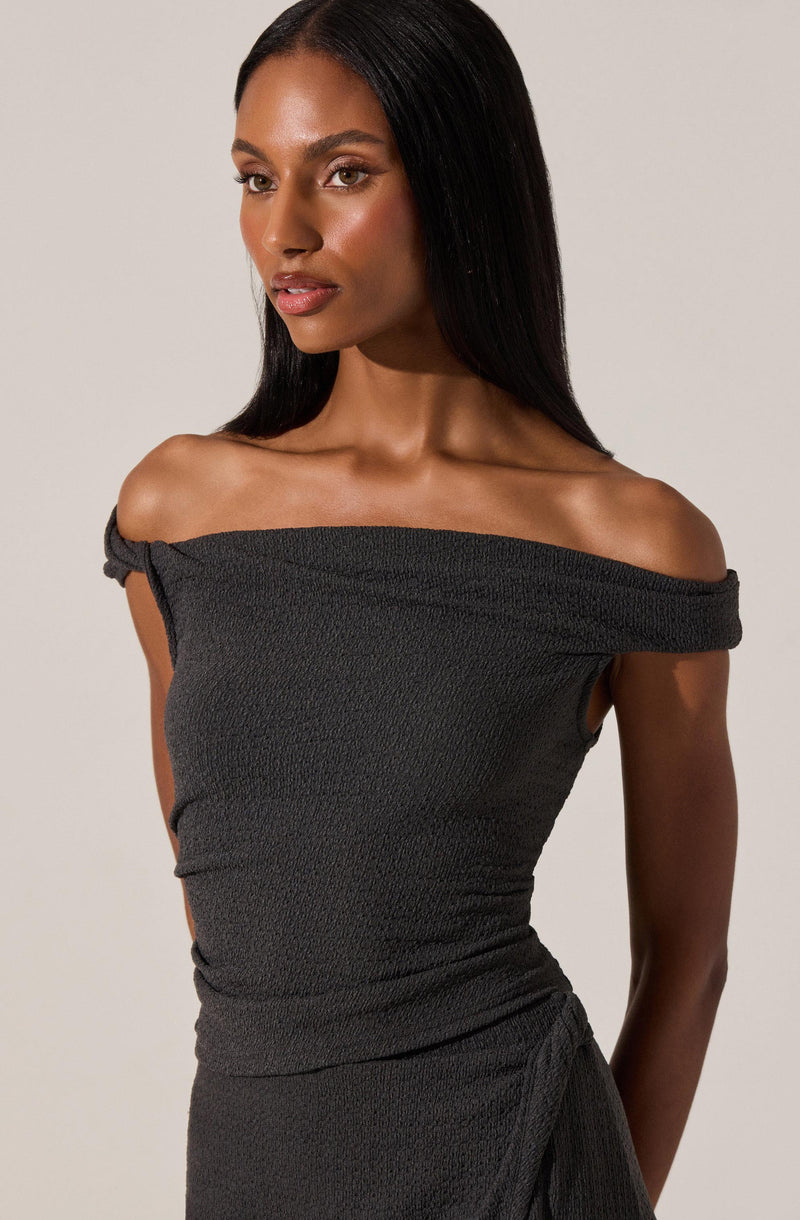 A woman is wearing a dark gray, off-the-shoulder dress made from a textured fabric. The dress features a wide neckline that drapes slightly over her shoulders and has a gathered, ruched appearance around the waist.