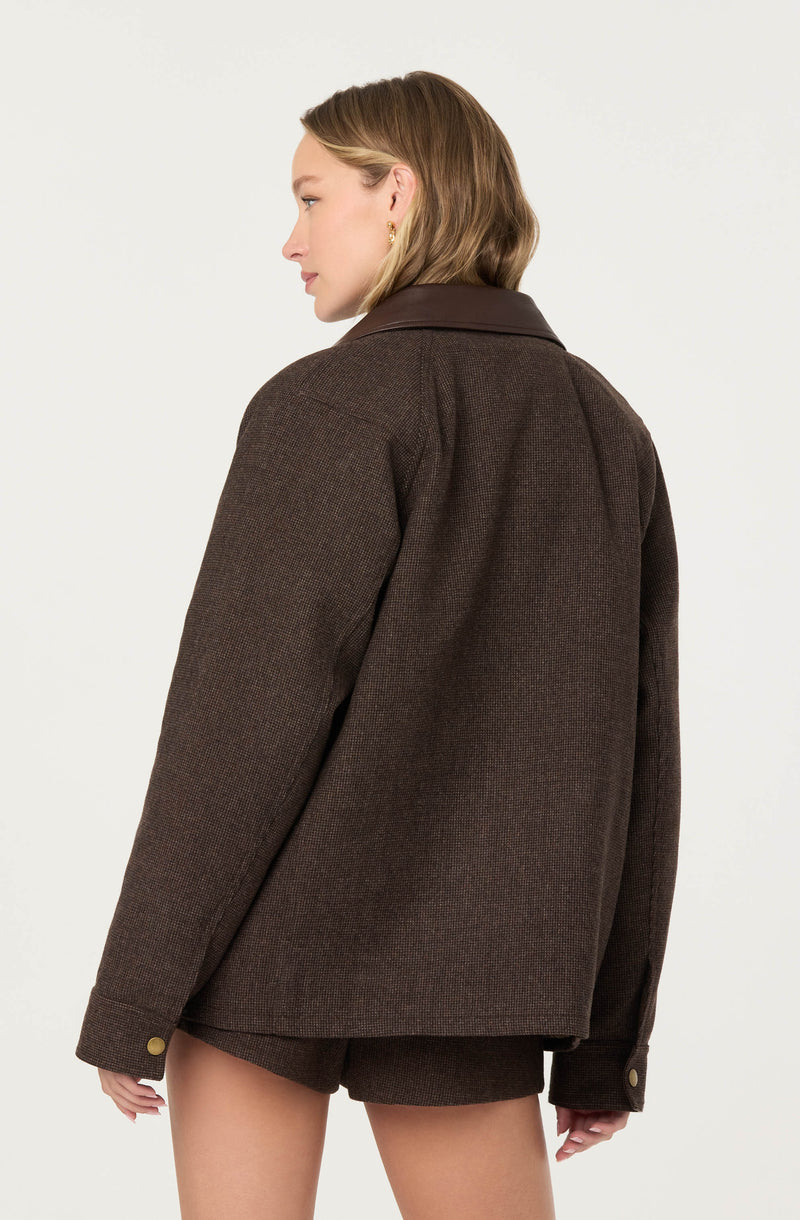 A woman is wearing a dark brown, textured wool jacket with a wide collar and buttoned cuffs. She is also wearing matching brown shorts. The jacket has a loose fit and appears warm and stylish.