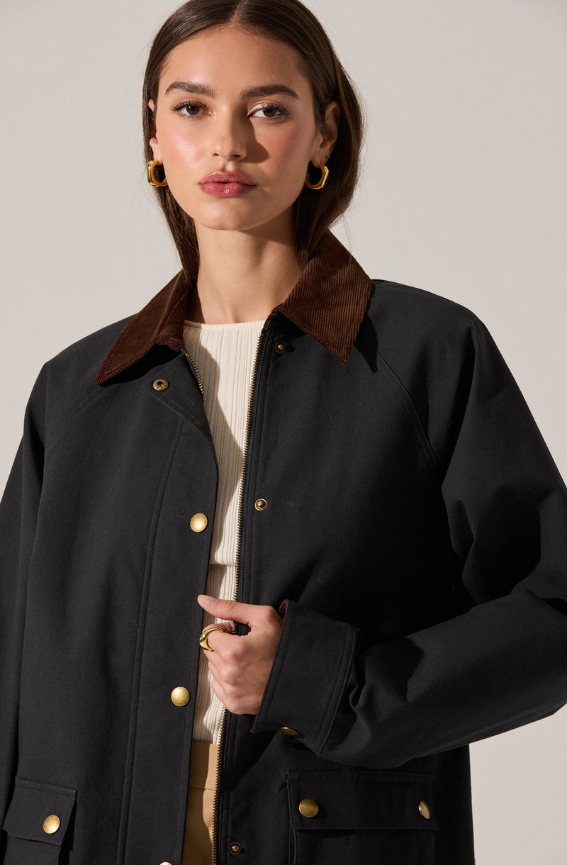 The image shows a woman wearing a black jacket with a brown corduroy collar and gold buttons. Underneath, she has on a cream-colored knit sweater.