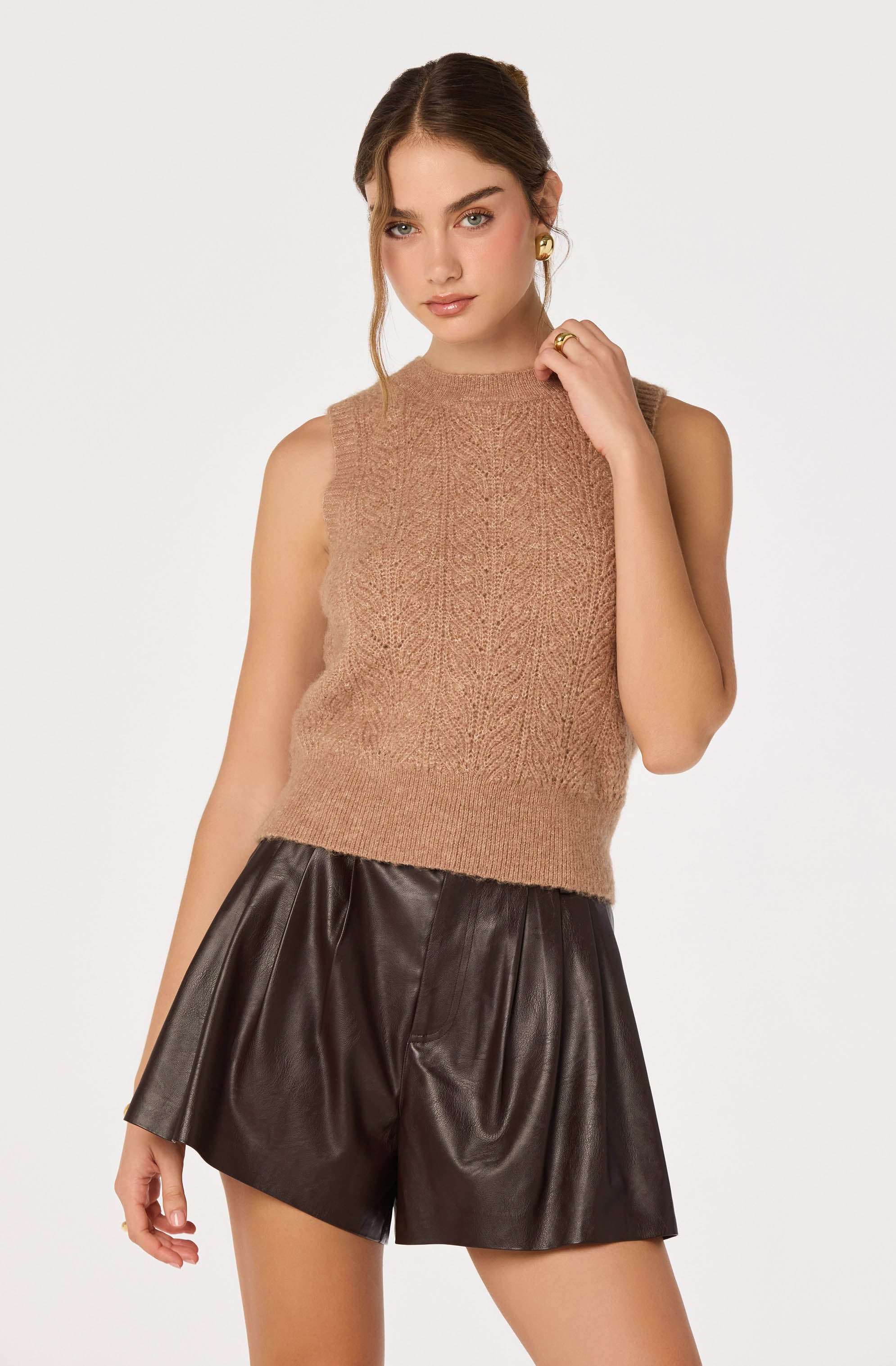 Sleeveless beige knit sweater with frayed armholes, paired with shiny black leather shorts.