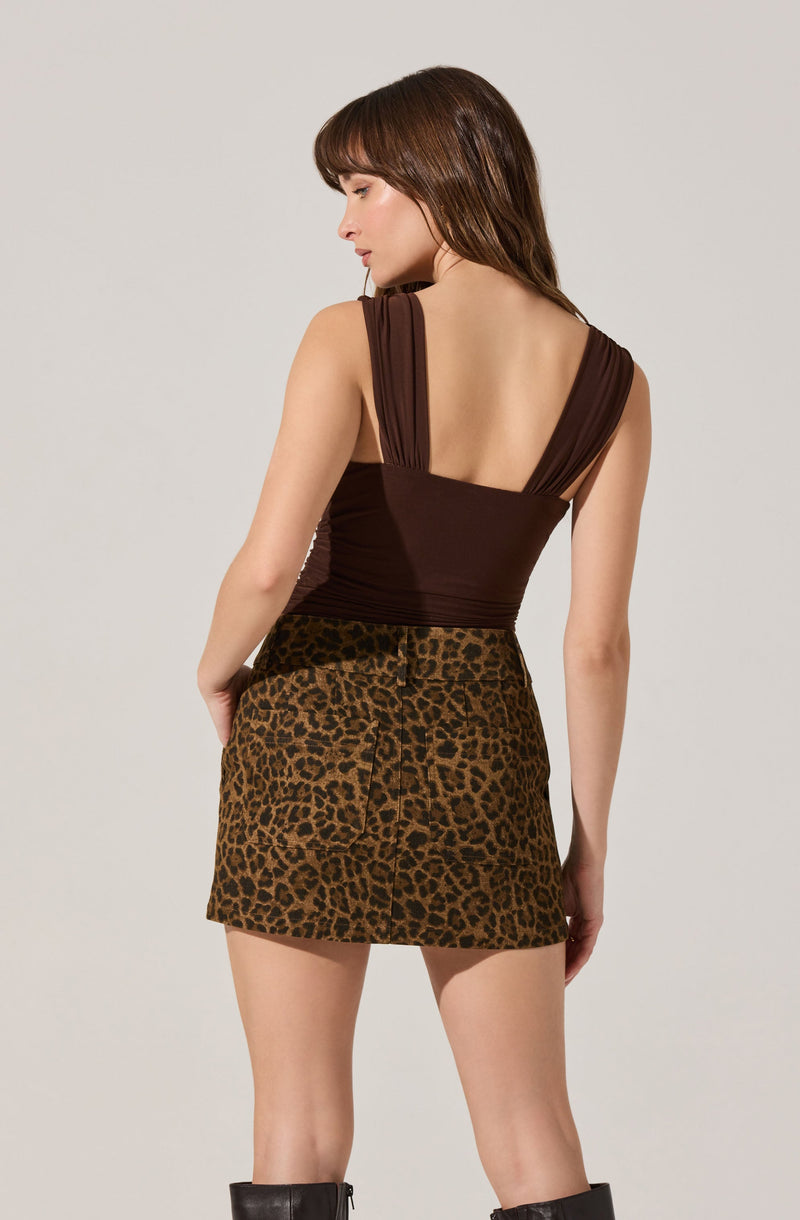 A woman is wearing a sleeveless, dark brown top with wide shoulder straps and a deep scoop back, paired with a high-waisted, leopard print mini skirt.