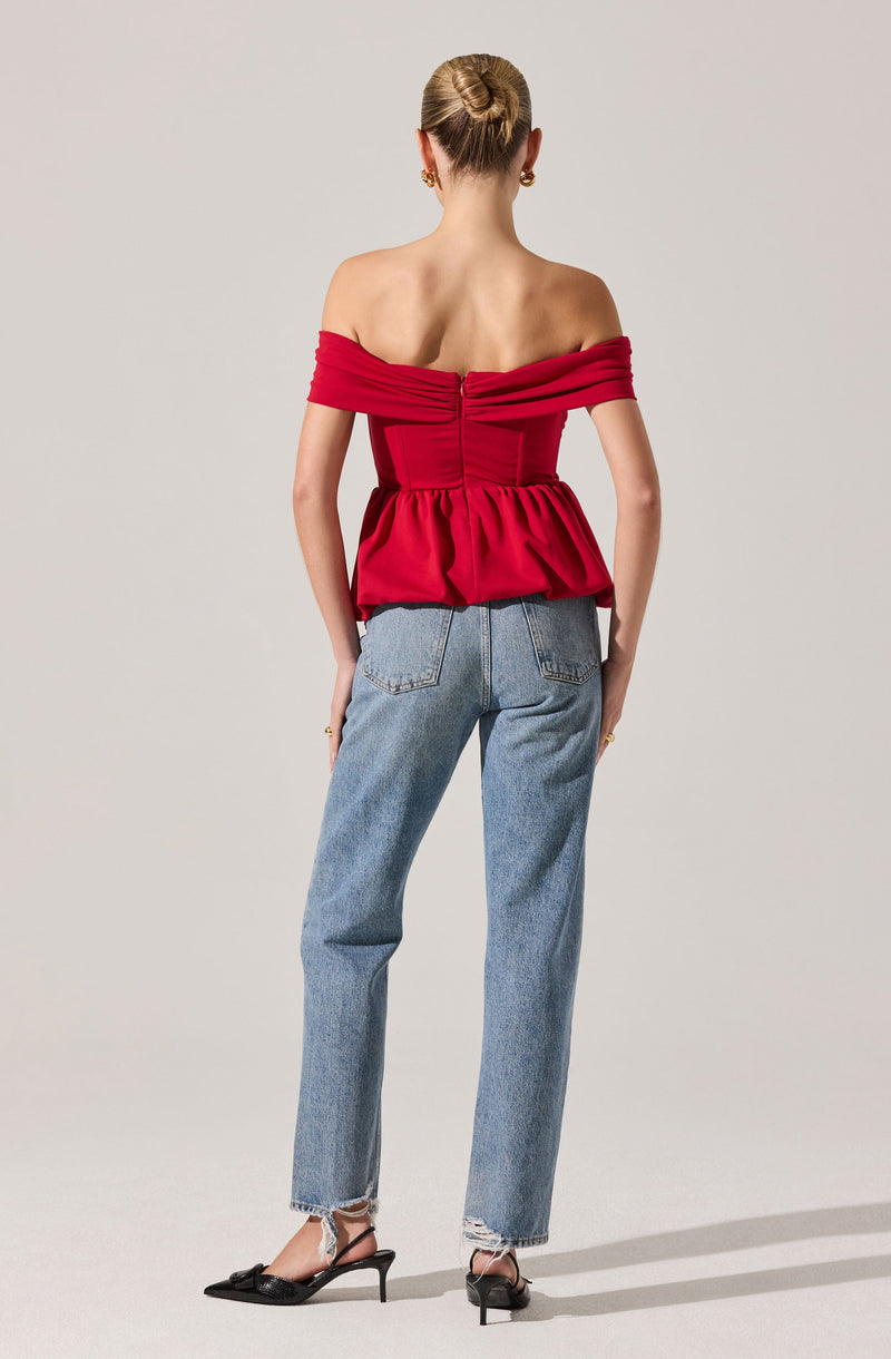 A person is wearing an off-the-shoulder red top with gathered fabric and a ruched detail at the back, paired with high-waisted, light blue, straight-leg jeans. They are also wearing black pointed-toe heels with ankle straps.
