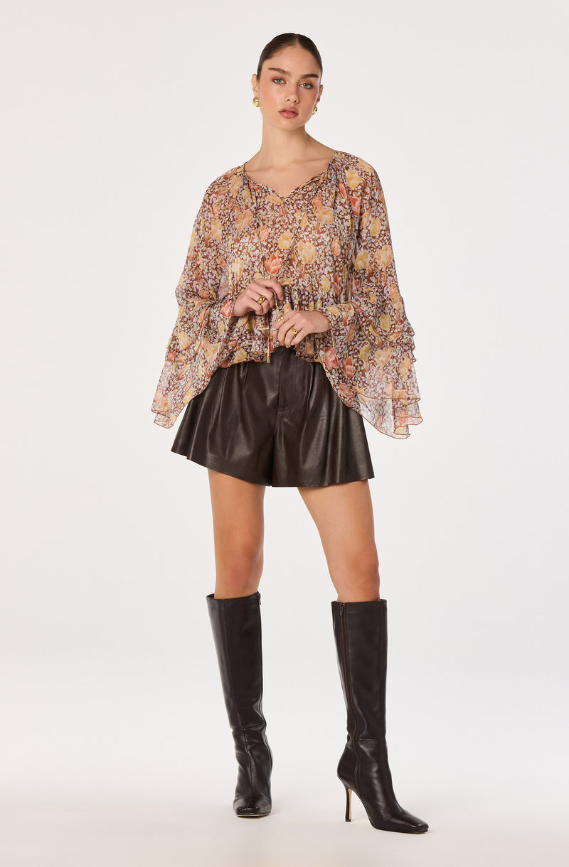 Woman wearing a flowy, floral patterned blouse, black leather shorts, and tall black boots.