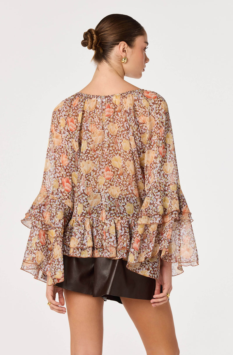 Woman in flowy, floral print blouse with ruffled sleeves and hem, paired with a black leather skirt.