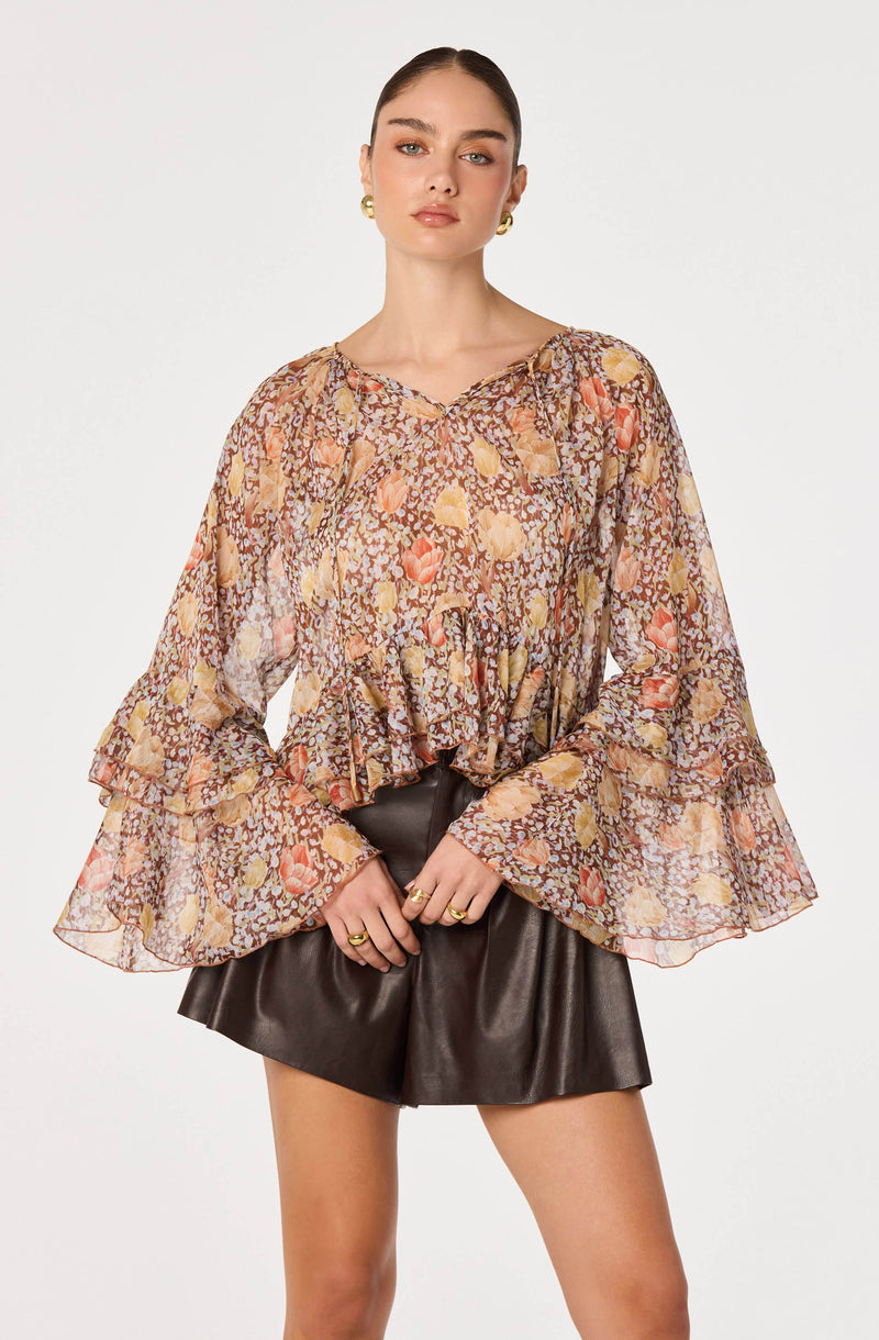 Sheer floral blouse with ruffled long bell sleeves and black leather shorts.