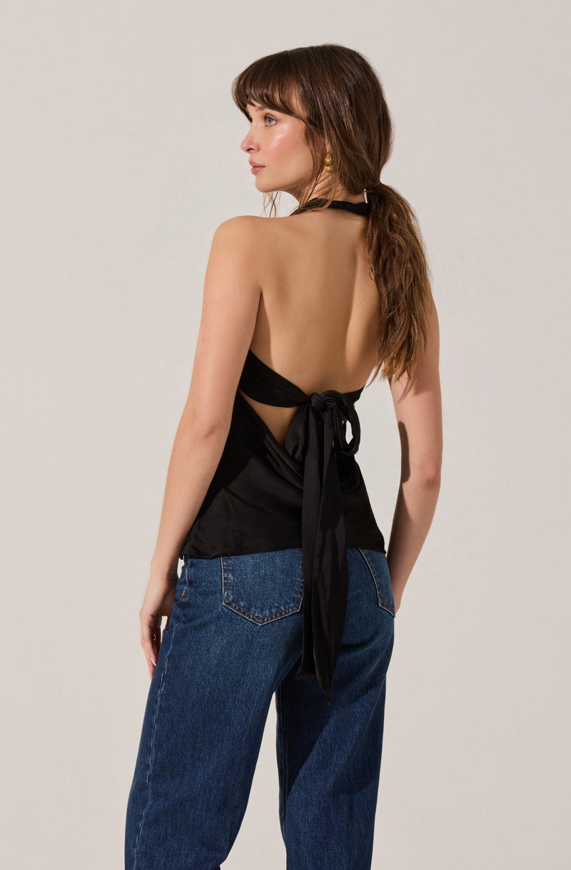 A woman is wearing a black halter-style top with a back tie detail, exposing her upper back. She is also wearing high-waisted blue jeans with visible stitching on the pockets.