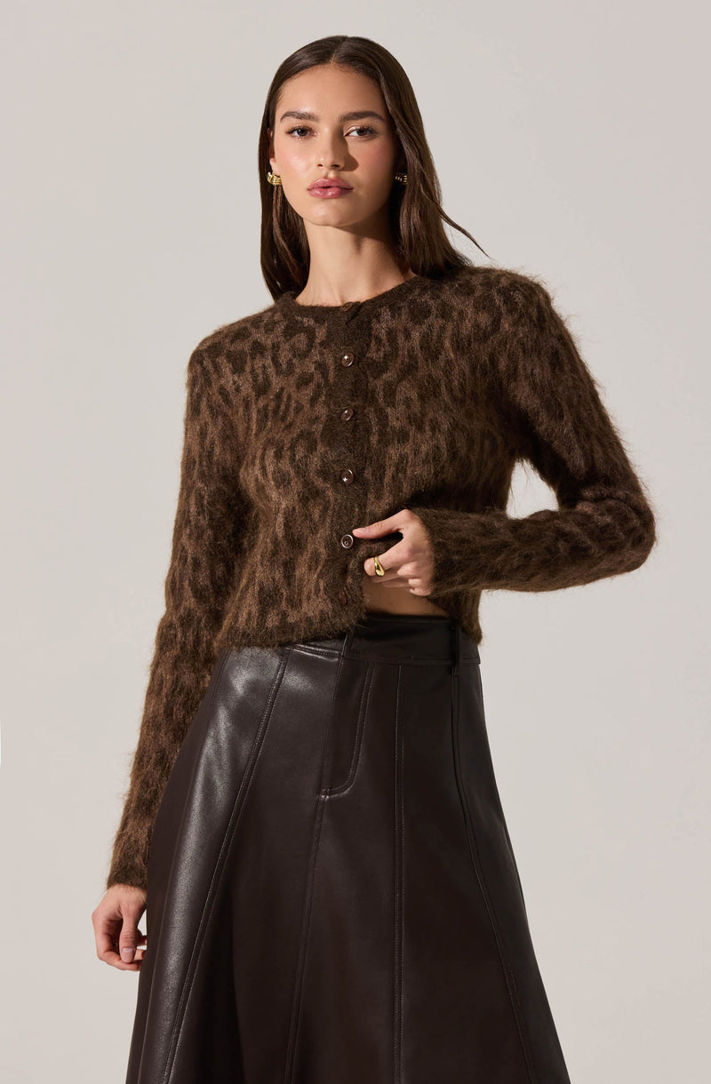 A woman is wearing a cropped, long-sleeve cardigan with a brown leopard print pattern and buttons down the front. She pairs it with a high-waisted, black, A-line leather skirt.
