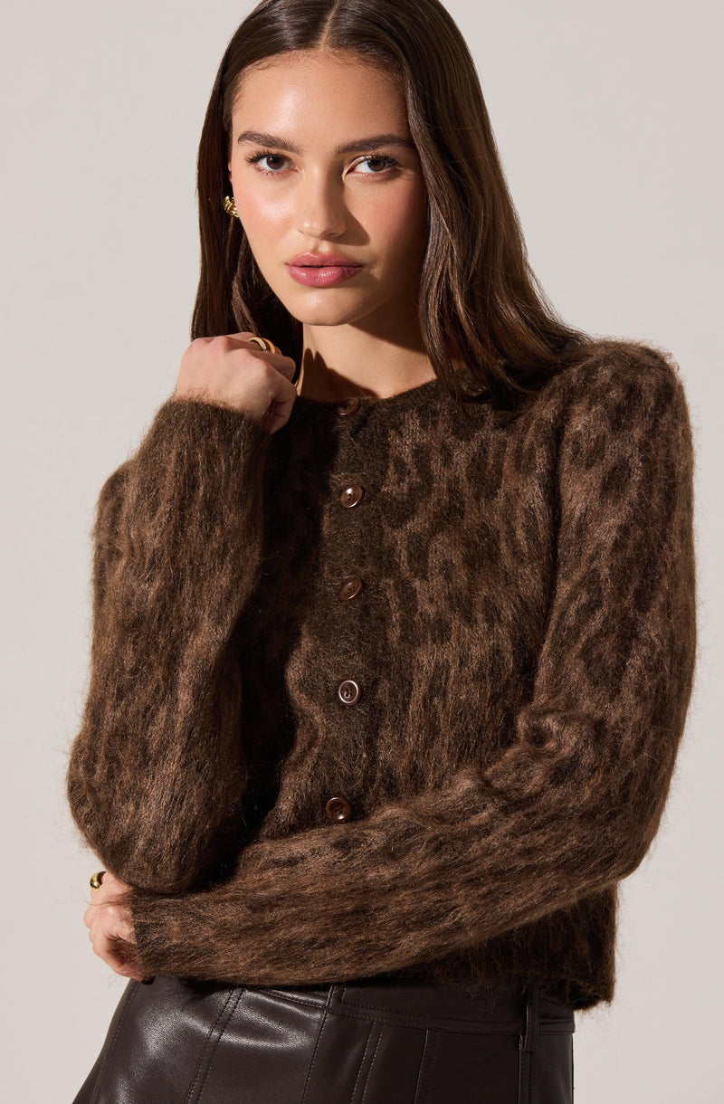 A woman is wearing a dark brown, fuzzy, button-up cardigan with a subtle leopard print pattern. The cardigan has a round neckline and is fastened with several buttons down the front. She is also wearing dark leather pants.