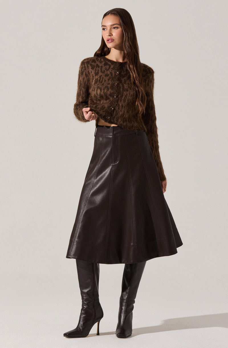 A woman is wearing a long-sleeved, button-up sweater with a brown and black leopard print pattern, paired with a high-waisted, A-line leather skirt that reaches below the knees. She is also wearing tall, black leather high-heeled boots.