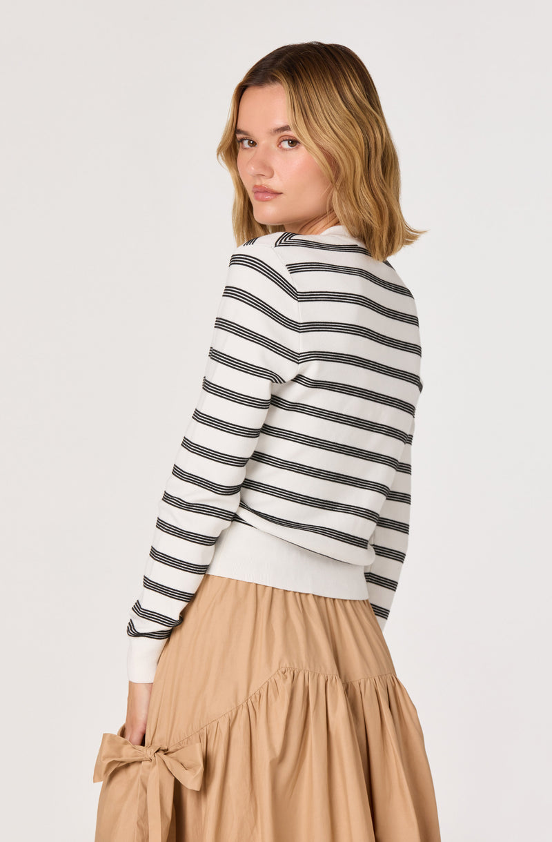 Woman wearing a white sweater with black horizontal stripes and a beige skirt with a bow.