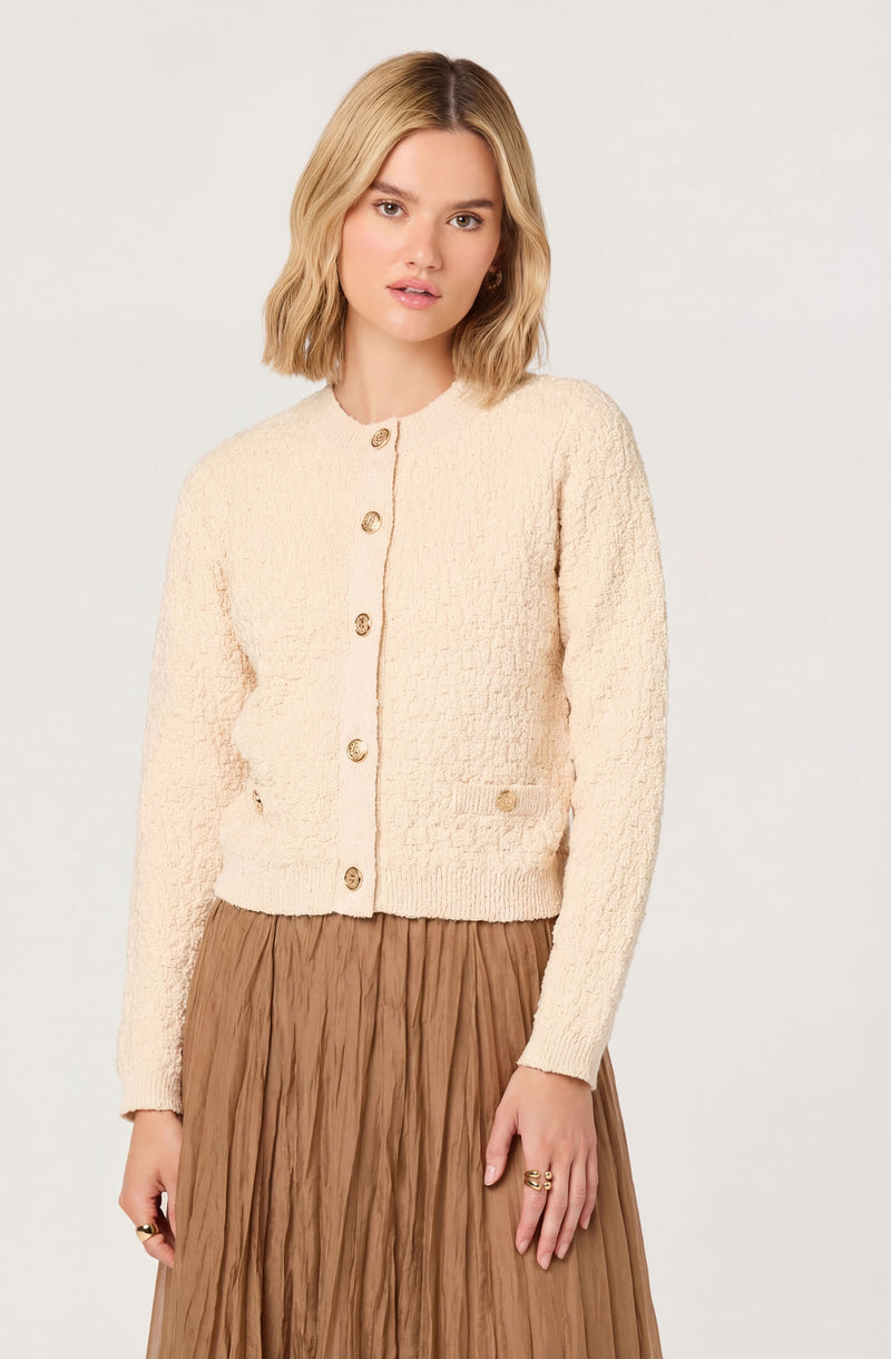 Female model wearing a cream textured button-up sweater and a brown pleated skirt.