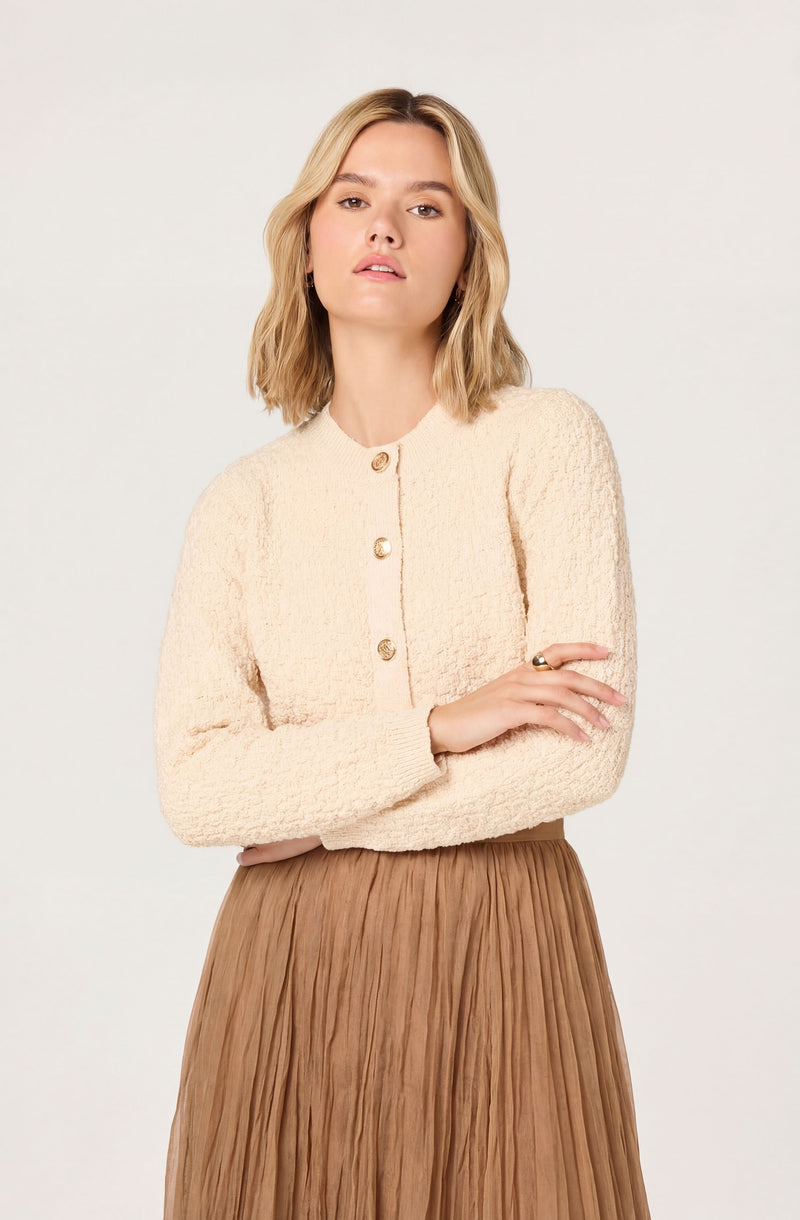 Cream textured cardigan with gold buttons, paired with a brown pleated skirt.