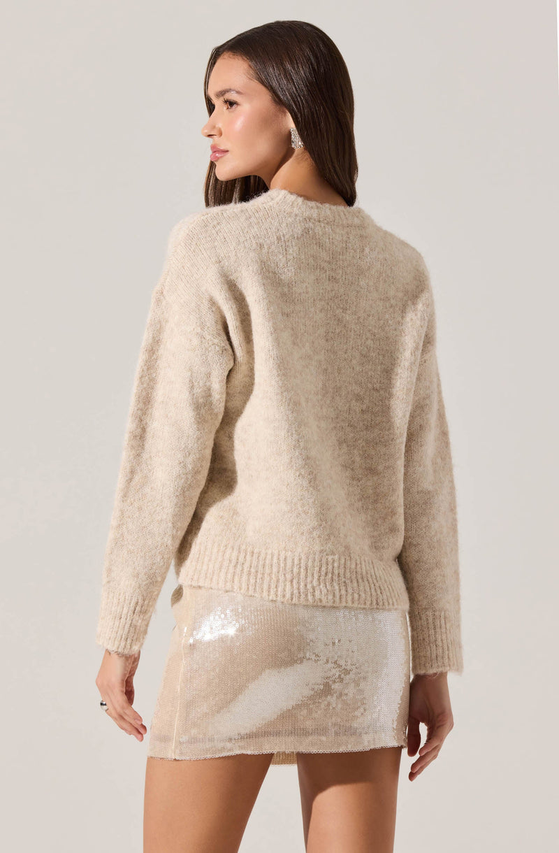 A woman is wearing a beige, fuzzy, long-sleeved sweater with a crew neckline and ribbed hem. She pairs it with a shiny, light-colored sequined mini skirt.