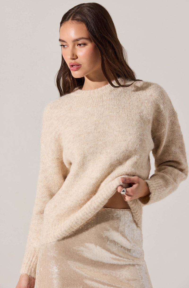 A woman wearing a loose, cream-colored fuzzy knit sweater with a round neckline and long sleeves. She is also dressed in a high-waisted, shimmery beige skirt that appears to be made of a sequined or sparkly fabric.