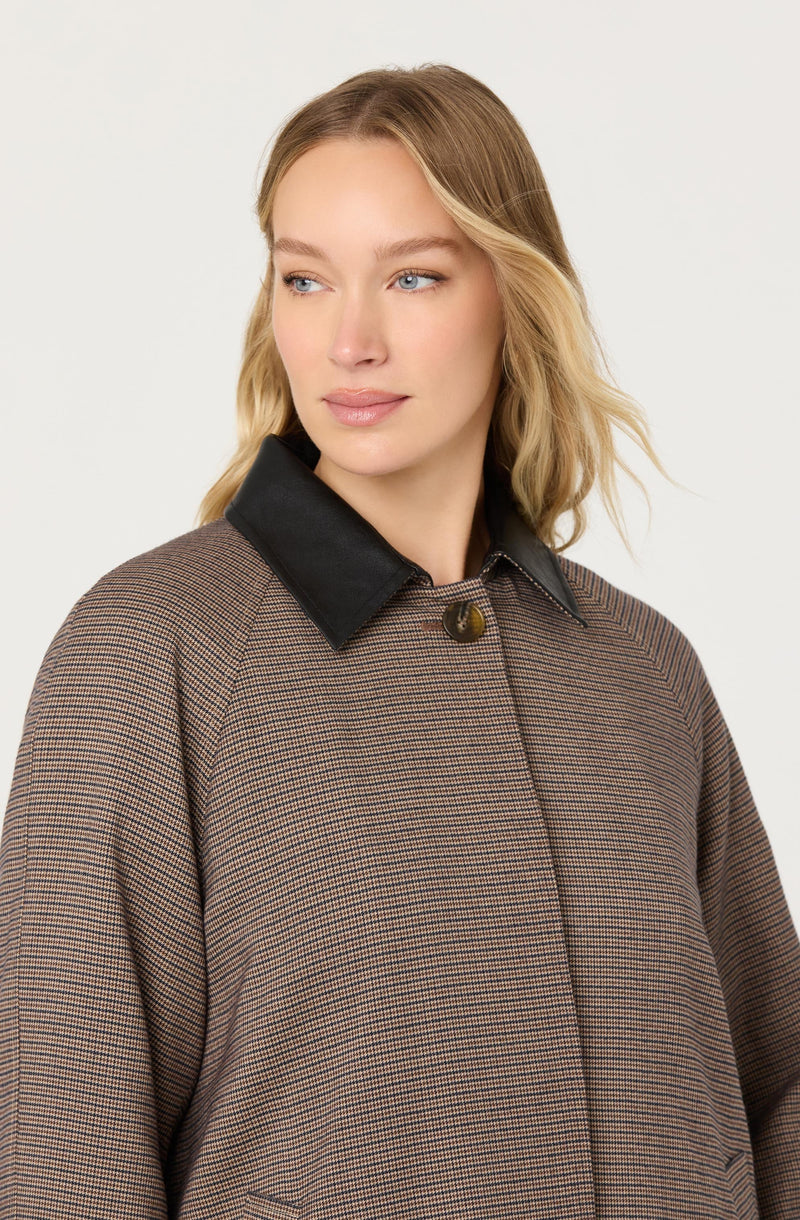 A woman is wearing a brown checked coat with a black leather collar and a single visible button at the top.