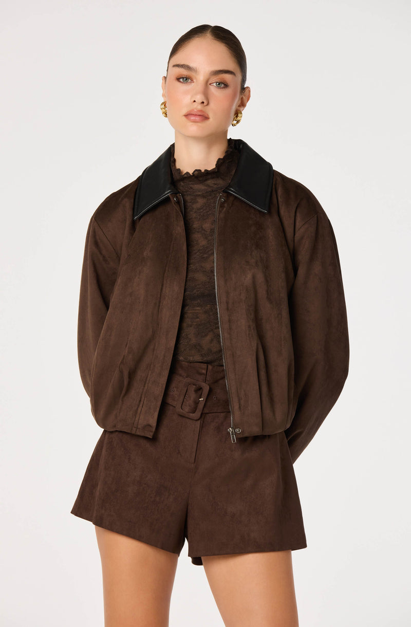 Woman wearing a brown bomber jacket with black collar and matching brown shorts.