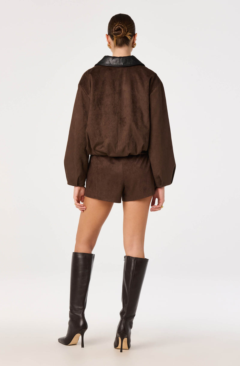 Woman in a brown suede jacket with black leather collar, matching suede shorts, and tall black leather boots.