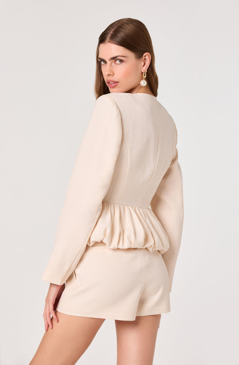 Woman in a beige blazer with puffed waist and matching shorts.