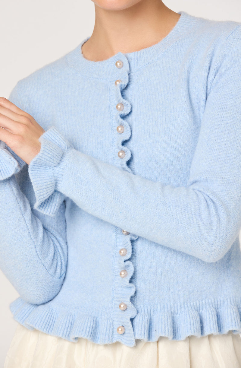 A light blue knit cardigan with pearl buttons down the front, featuring a ruffled hem and ruffled cuffs on the sleeves.