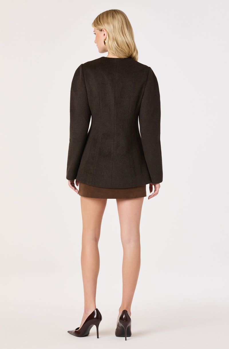 Woman wearing a dark jacket, brown skirt, and high heels, facing away.
