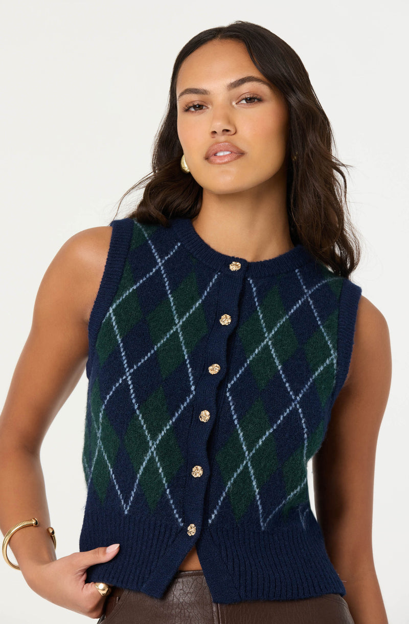 A woman is wearing a sleeveless knitted vest with an argyle pattern in navy blue, dark green, and light blue, featuring gold button closures down the front.