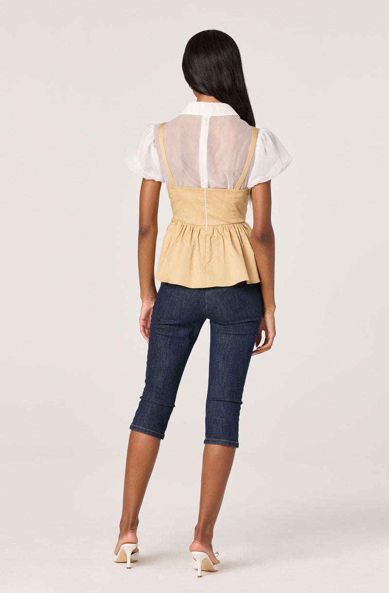 A woman is wearing a white short-sleeve blouse with puffed sleeves, layered under a beige sleeveless peplum top with a fitted waist and a ruffled hem. She is also wearing dark blue capri jeans and beige high-heeled sandals.
