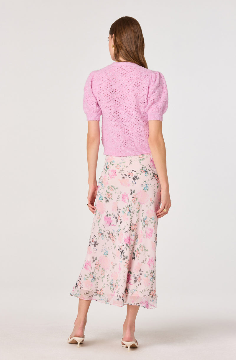 Woman wearing a pink knitted short-sleeve sweater with puff shoulders and a long, floral skirt.