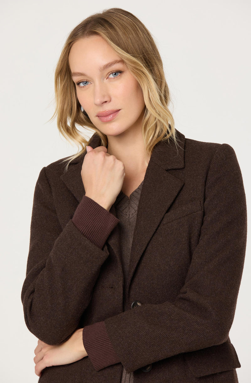 Woman in a dark brown blazer with ribbed cuffs and matching sweater.