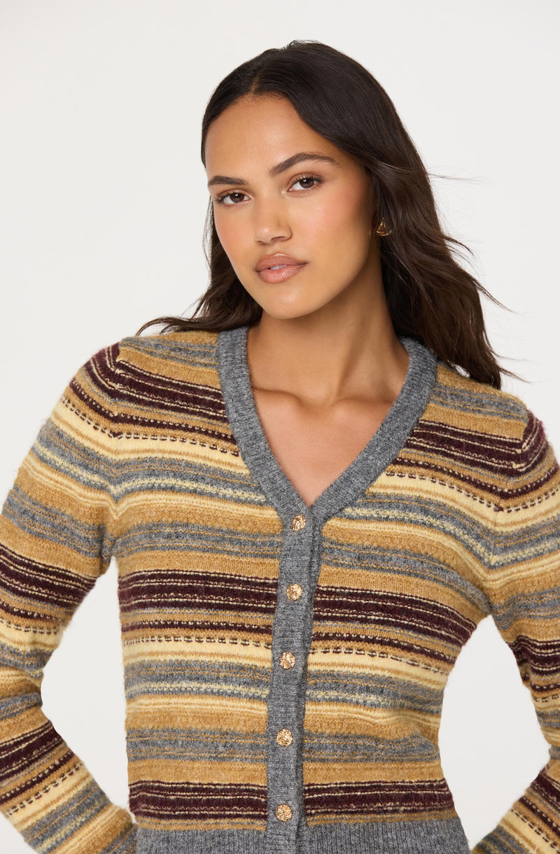 A woman is wearing a button-up sweater with horizontal stripes in shades of mustard yellow, beige, gray, and burgundy. The sweater has a gray trim around the collar, down the front, and at the hem.