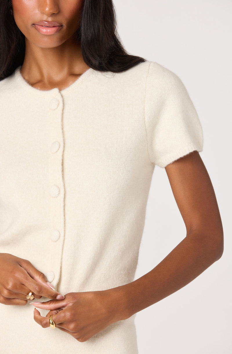 Woman wearing a short-sleeve, cream-colored, button-up sweater.