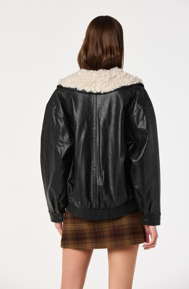 Woman wearing a black leather jacket with a white faux fur collar and a brown plaid skirt.