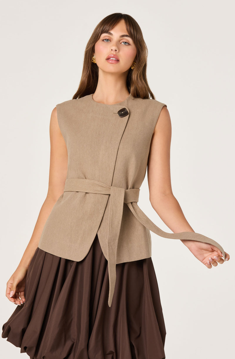 Beige sleeveless vest with large shoulder pads, tied at the waist with a matching belt, paired with a dark brown skirt.