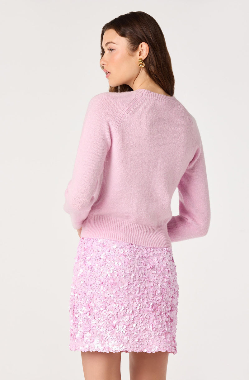 Woman in a pink sweater and a pink textured skirt, facing sideways.