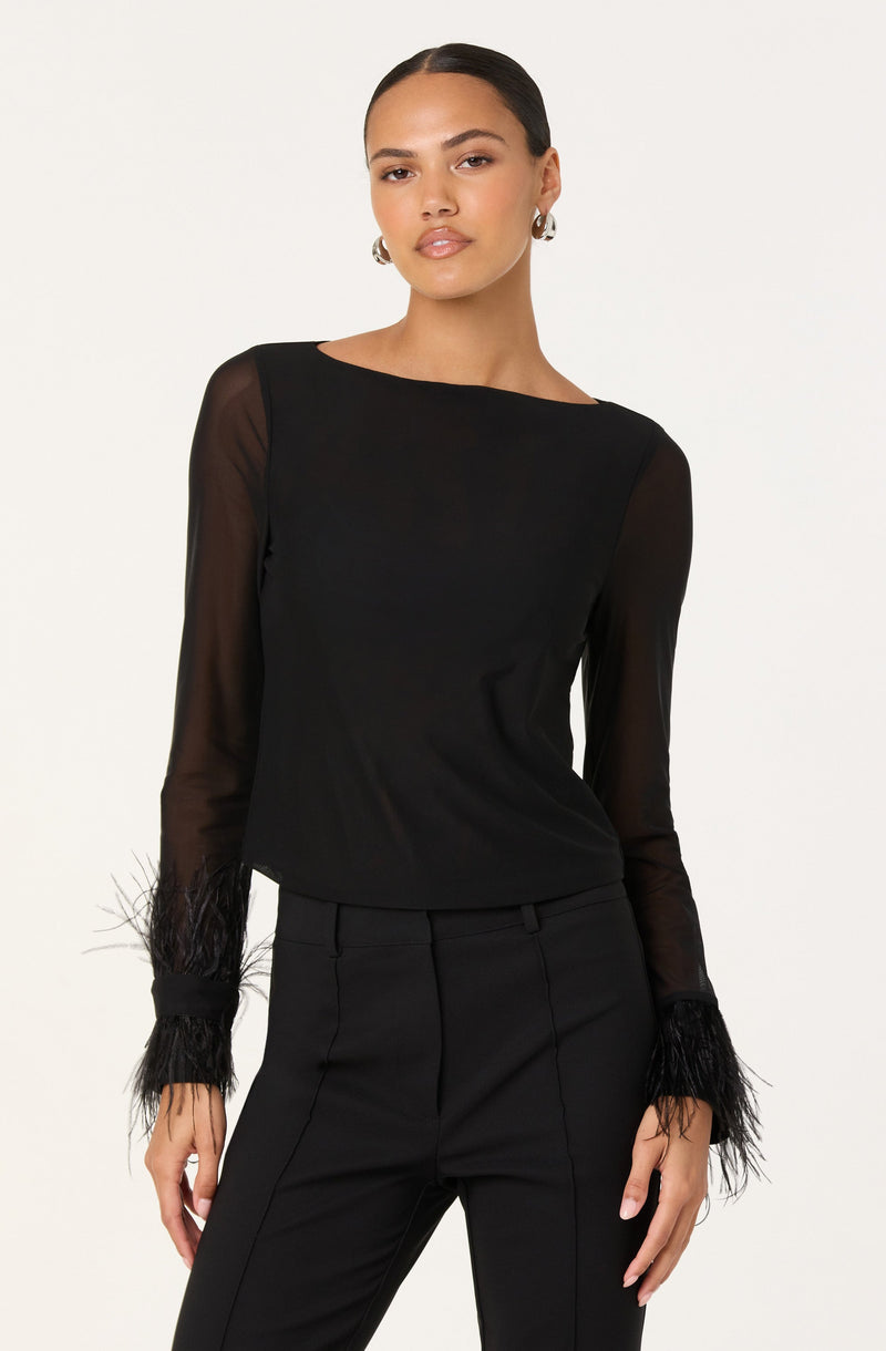 A woman is wearing a black long-sleeve top with sheer sleeves and feathered cuffs. She pairs it with black tailored pants.