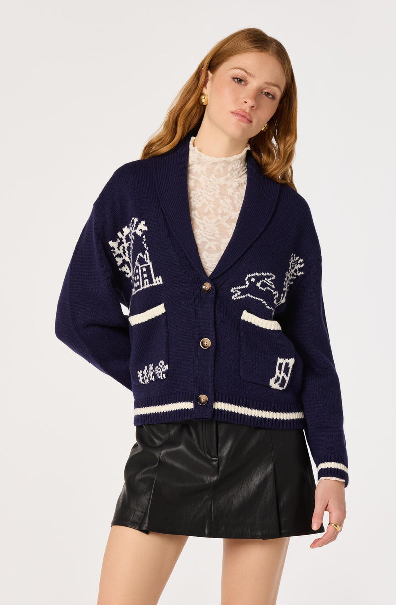 Woman wearing a navy blue cardigan with white patterns, paired with a cream lace top and a black leather skirt.