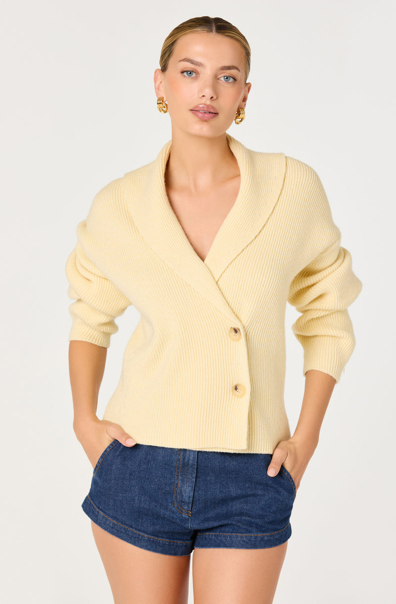 Woman wearing a cream knitted cardigan with large collar and blue denim shorts.