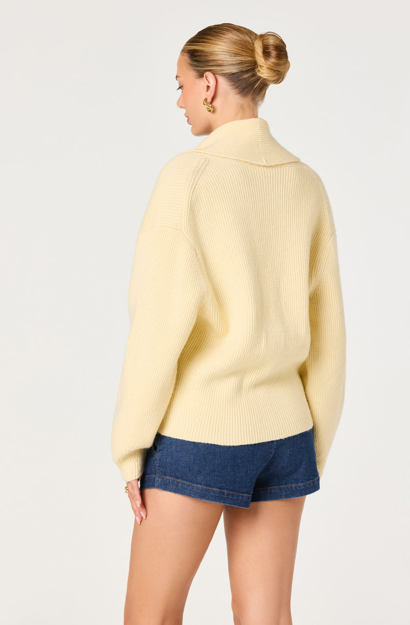 Woman wearing a cream oversized knit sweater and dark denim shorts.