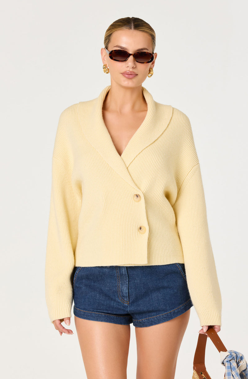 Woman wearing a cream chunky knit cardigan with large buttons and denim shorts.