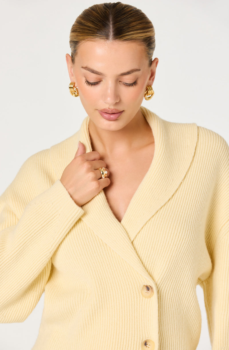 Woman in a yellow, ribbed, button-up cardigan with large gold hoop earrings and a gold ring.