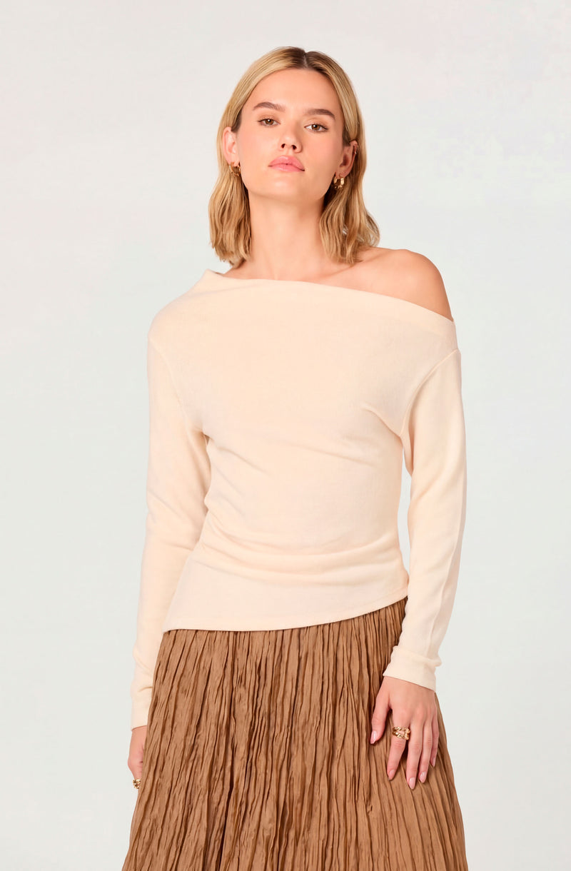 Off-the-shoulder cream sweater with long sleeves and a pleated brown skirt.