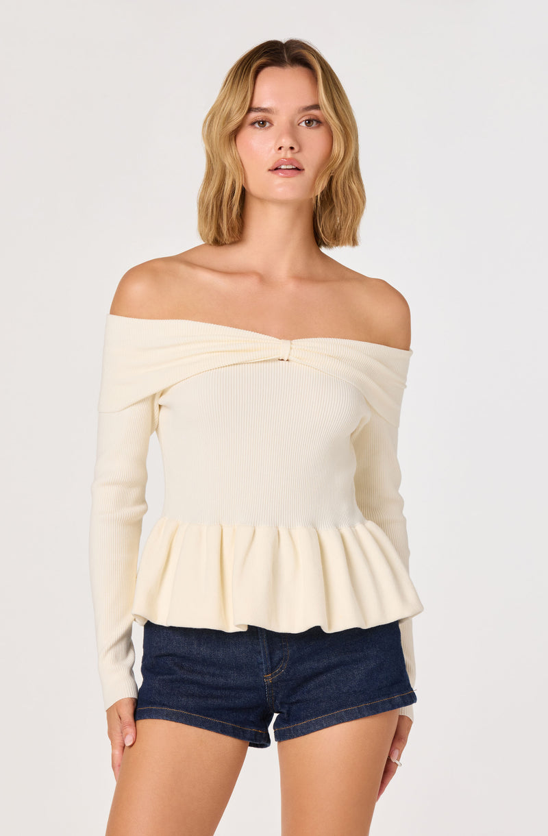 Off-shoulder cream sweater with ruffled hem and long sleeves, paired with dark denim shorts.