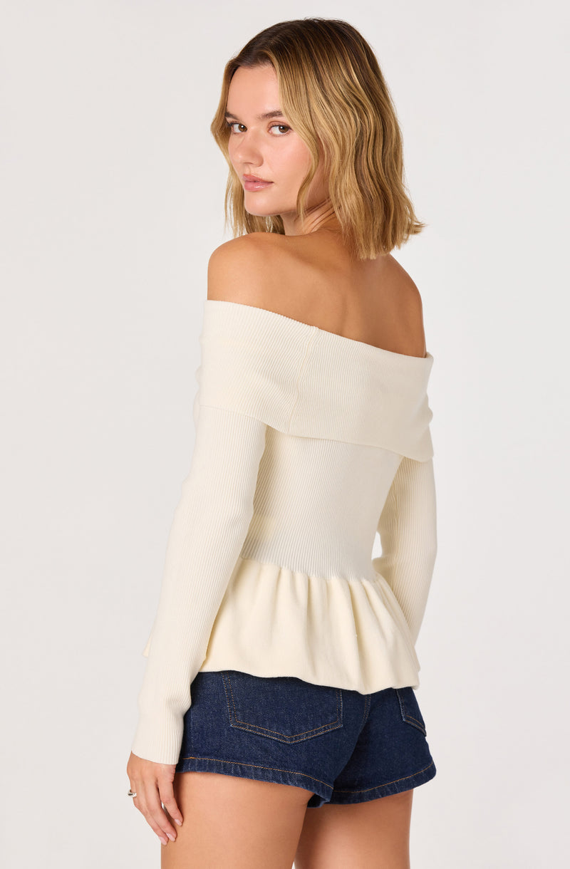 Off-the-shoulder cream sweater with ruffled hem paired with dark denim shorts.